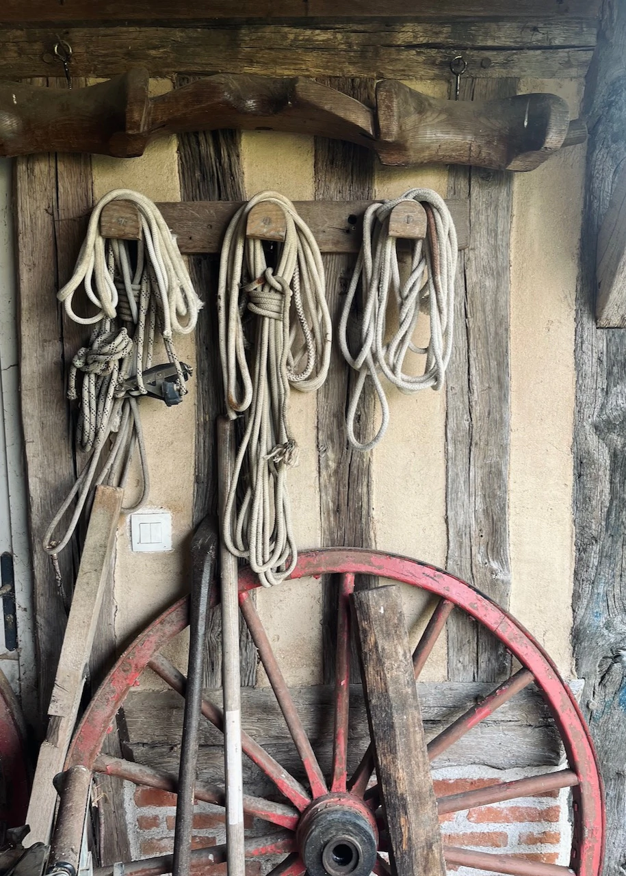 Cordes suspendues et vieille roue de charrette rouge, accrochées au mur en pans de bois d'une grange